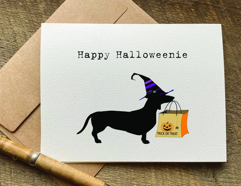 a card with a Weiner dog wearing a witches hat and holding a trick bag saying happy halloweenie