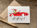 Christmas card with vintage graphic of Santa Claus driving a red car and the text 'sleighing it' 